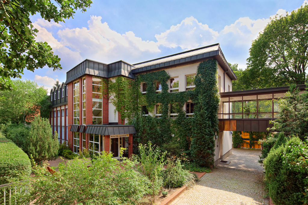 Außenansicht vom Hotel Morgenland, Haupteingang es ist sehr grün, die Sonne scheint, , ein paar Wolken sind zusehen