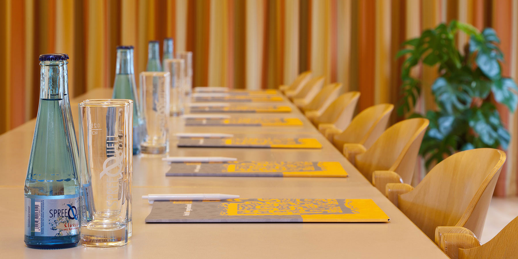 Foto von einem Seminarraum die Tische sind eingedeckt mit Getränken, Gläsern, Blöcke, rechts gibt es Fenster mit Vorhängen