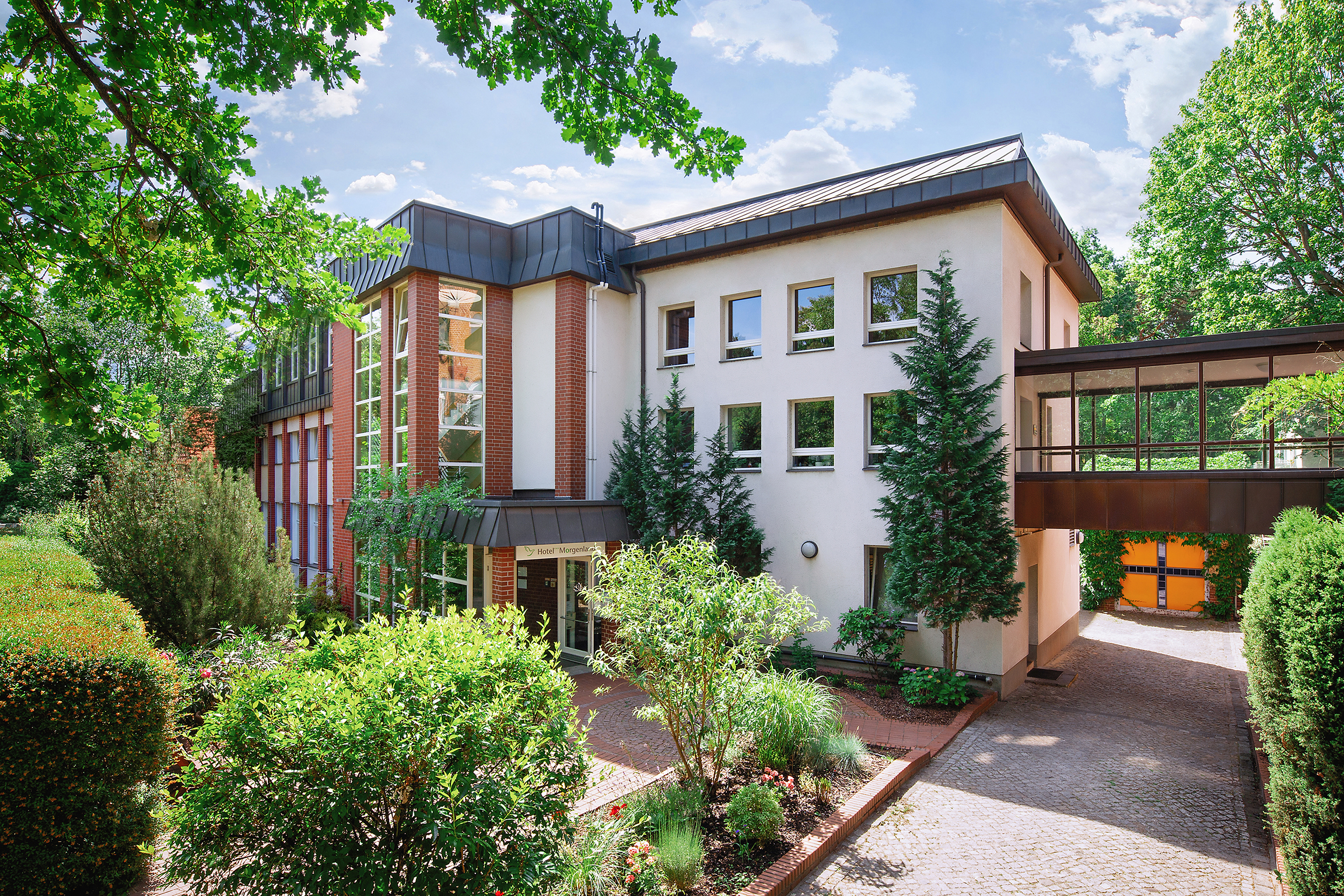 Außenansicht vom Hotel Morgenland, Haupteingang es ist sehr grün, die Sonne scheint, , ein paar Wolken sind zusehen 2018