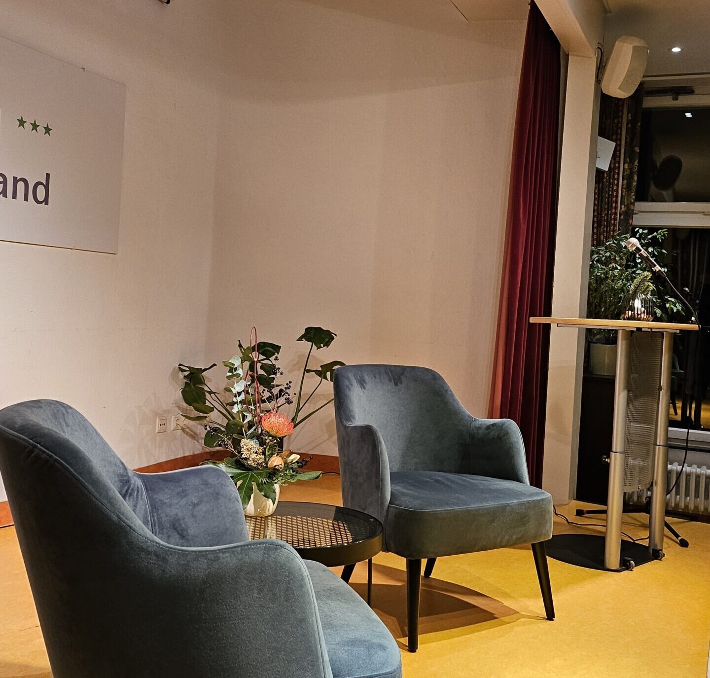 zwei Stühle auf der Bühne im Hotel Morgenland bei einer Podiumsdiskussion, dazwischen ein Tisch mit Blumen, im Hintergrund stehen grüne Pflanzen und ein Rednerpult