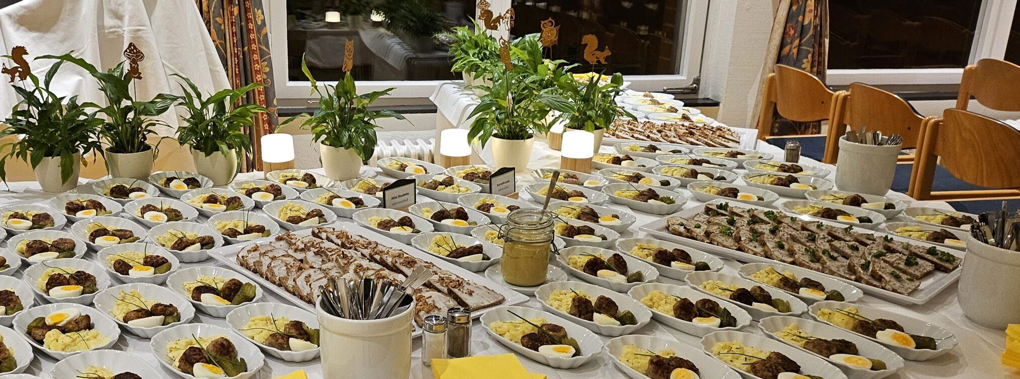 Buffett bei einer Lesung im Hotel Morgenland, mit vielen flache Porzellanschale und darauf befindend sich, Kartoffelsalat, Eier, Gurken, Bouletten, im Hintergrund stehen Lichter und Pflanzen